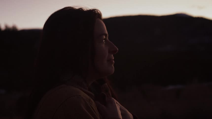 Close up of a thoughtful woman lifting her head to gaze at the mountain landscape at twilight