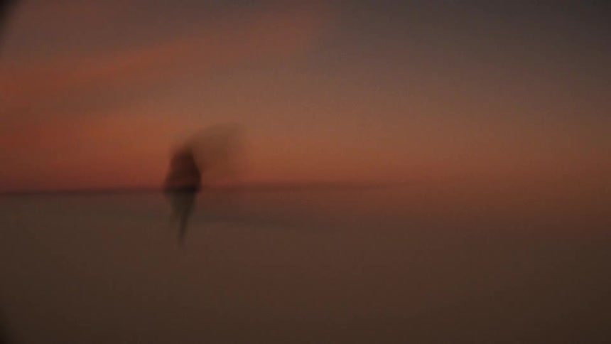 A shaky, out-of-focus shot of silhouetted people walking and dancing in a vast desert landscape at sunset