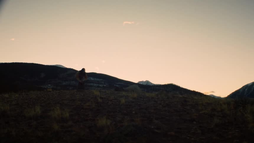 A lone hiker pauses on a silhouetted ridge to photograph the majestic mountain range at sunset