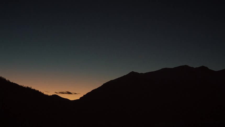 The last light of day glows on the horizon behind a silhouetted mountain range at dusk