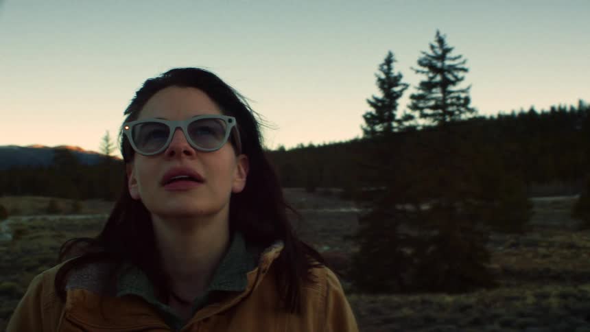 A thoughtful woman wearing sunglasses enjoys a peaceful moment in a vast mountain landscape at sunset