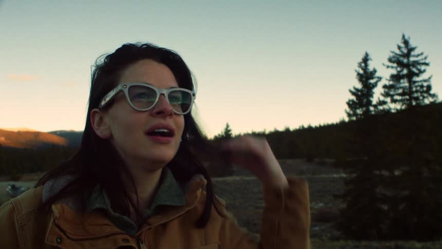 A thoughtful woman in glasses takes a moment to admire the sky in a tranquil mountain meadow at sunset in slow motion