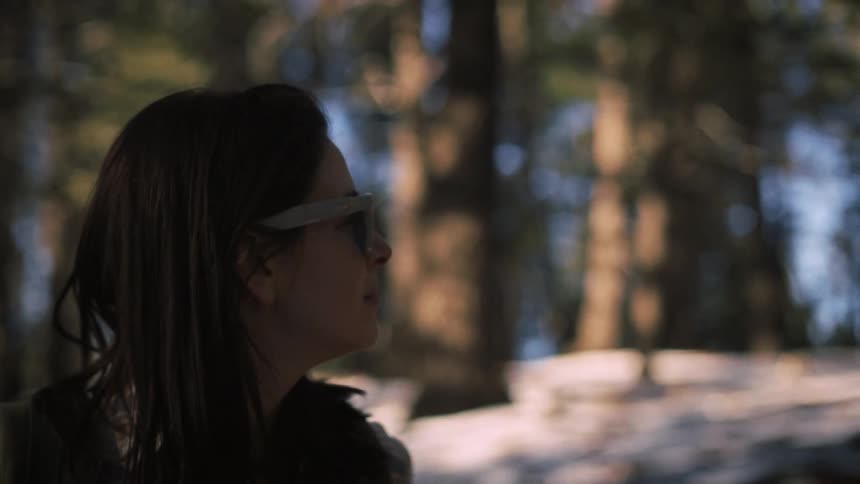 A contemplative woman wearing sunglasses admires the view in a snowy forest in slow motion