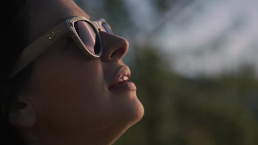 A serene woman wearing sunglasses enjoys a peaceful moment, looking up at the sky with a gentle smile at dusk