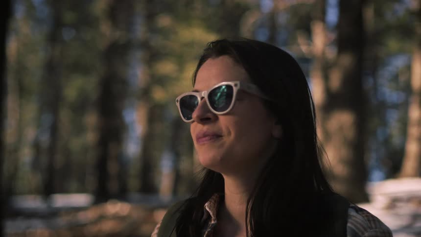 Close up of a woman in a winter forest whose smile fades into a look of thoughtful sadness
