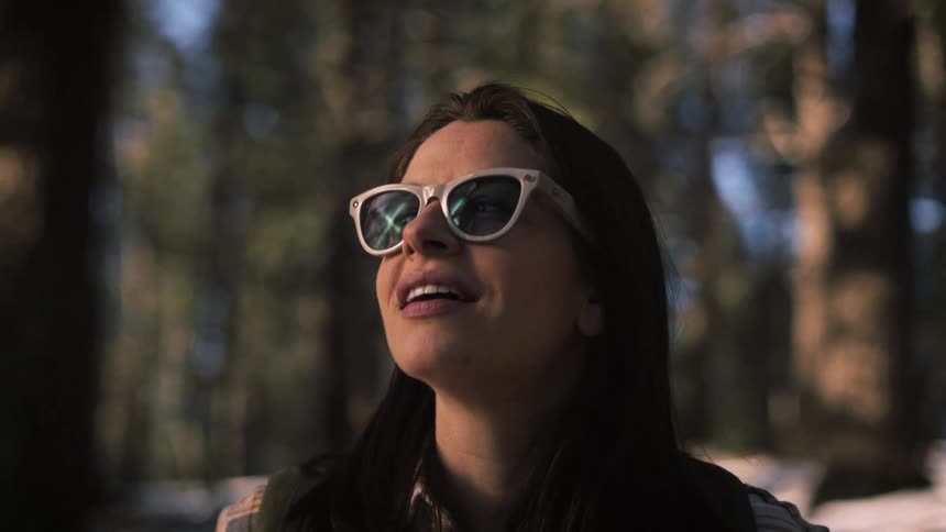 Slow motion close-up of a smiling woman in sunglasses looking up at the trees in a snowy forest