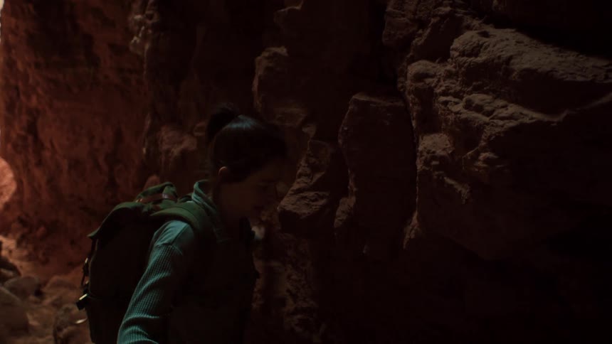 A female adventurer cautiously hikes through a dark and narrow slot canyon in slow motion