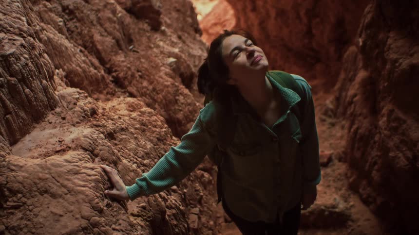 Slow motion shot of an amazed female hiker looking up towards the light inside a beautiful red rock slot canyon