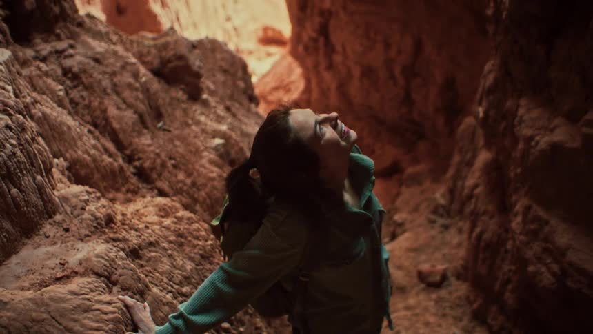 Slow motion shot of an adventurous woman looking up at the light filtering into a beautiful slot canyon