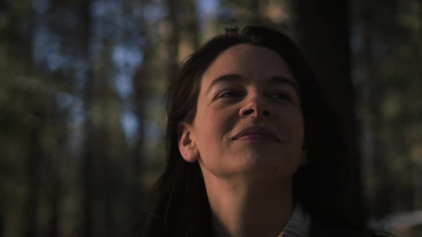 A serene woman closes her eyes and breathes deeply, finding a peaceful moment of connection with nature in a sunlit forest
