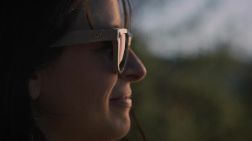 Close-up profile of a woman smiling in sunglasses as her hair blows in the wind during a serene golden hour