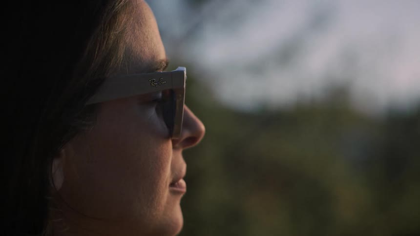 A contemplative woman wearing sunglasses looks off into the distance in a serene profile shot during golden hour