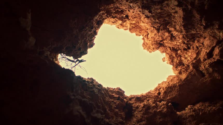 A low-angle shot from inside a cave reveals a heart-shaped opening to the sky above