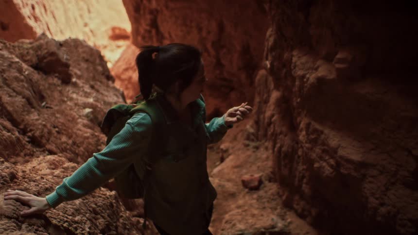 A smiling young woman explores the inside of a narrow, red rock slot canyon in slow motion