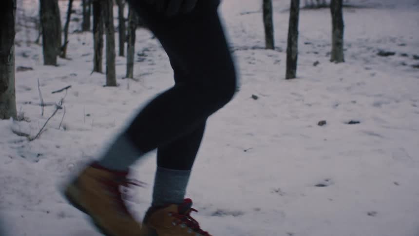 A close-up slow-motion shot of hiking boots walking through a snowy forest