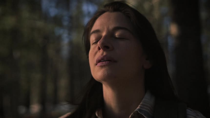 A young woman closes her eyes and takes a deep breath of fresh air in a tranquil forest at sunset