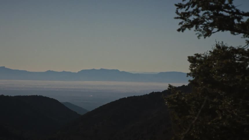 A majestic, layered view of silhouetted mountain ranges with a hazy valley floor in the distance