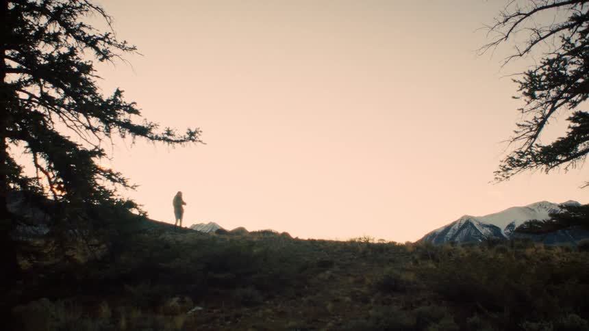 A lone hiker, silhouetted against the warm glow of sunset, pauses on a ridge to admire the snow-capped mountains