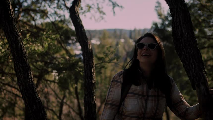 A happy female hiker pauses to admire the beautiful forest scenery on a sunny day before continuing her journey in slow motion