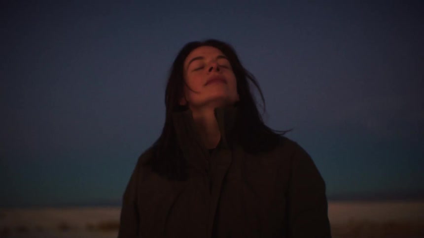 A serene woman gazes at the twilight sky, closing her eyes to peacefully absorb the moment in slow motion