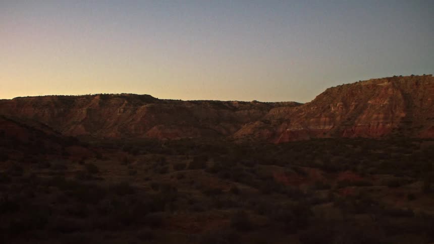 A slow pan reveals a vast desert canyon landscape with red rock formations at sunrise