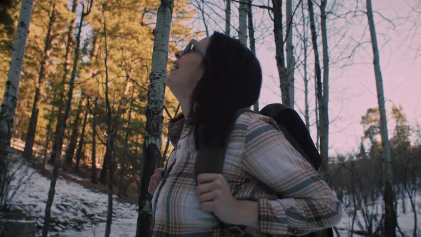 Slow motion shot of a joyful woman hiking in a snowy forest, stopping to look up and embrace the natural beauty around her