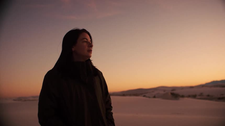 A contemplative woman stands in a vast white sand desert, peacefully observing the beautiful sunset