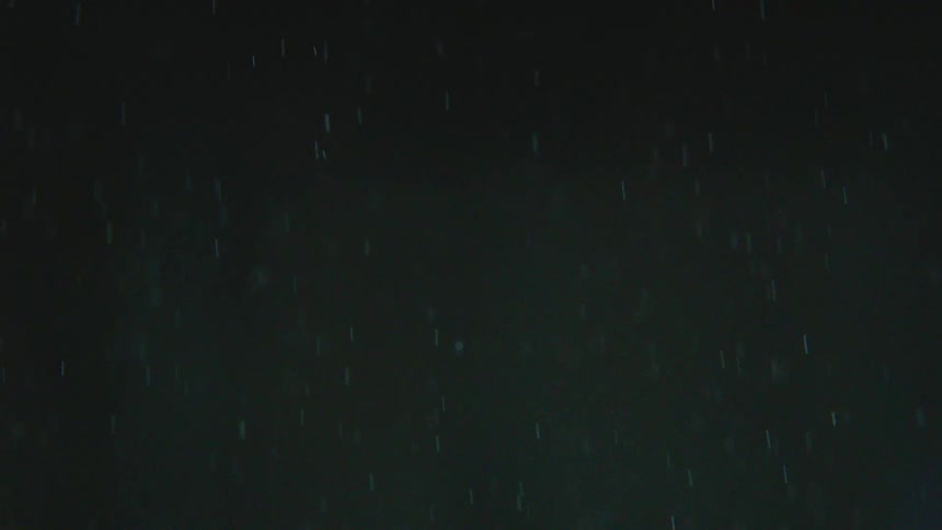 An abstract slow-motion shot of shimmering glitter and dust particles falling through the air against a dark background