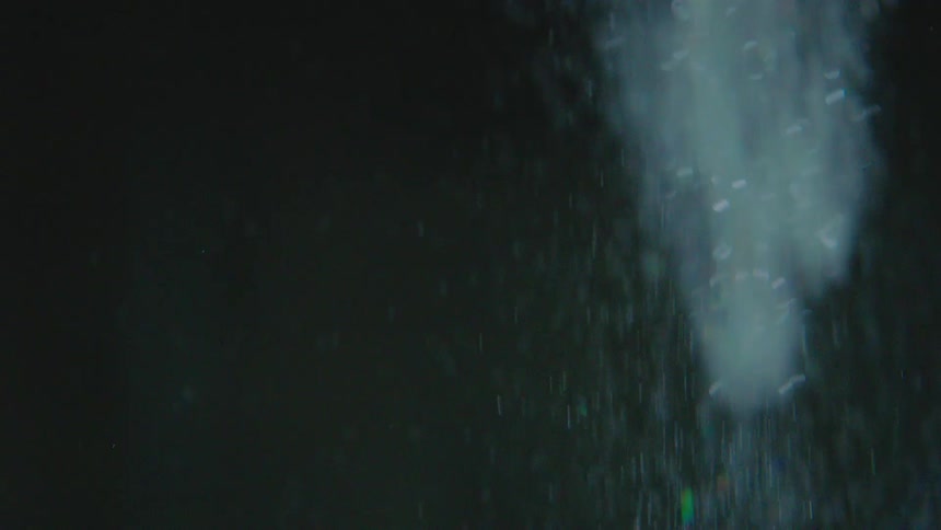 Shimmering glitter particles cascade through a dark, mysterious background in slow motion