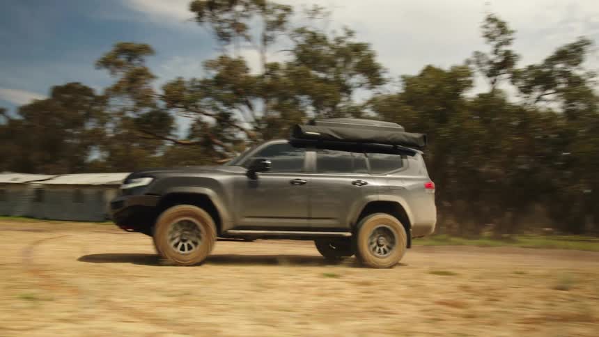 A rugged 4x4 vehicle equipped for adventure drives along a dusty track in a dry, rural landscape