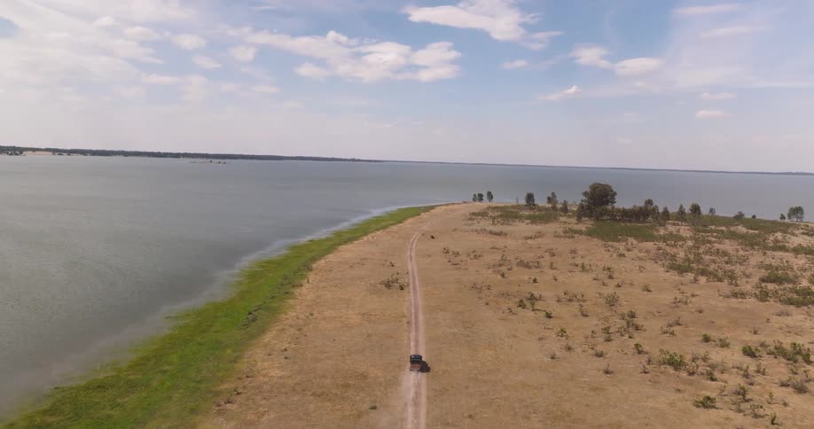 An aerial view captures an SUV driving along a dusty coastal road, kicking up dirt on a scenic adventure