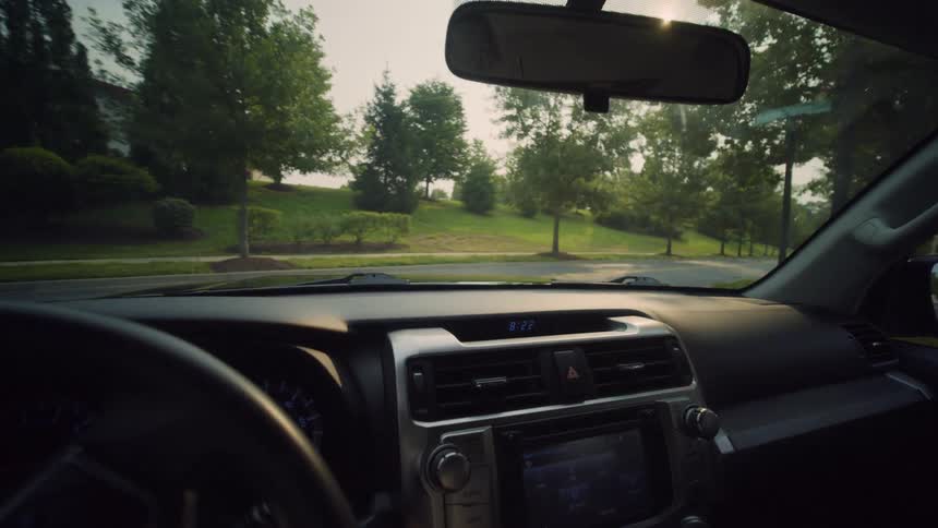 Driver's point-of-view shot of a car turning at an intersection and driving through a quiet, tree-lined suburban neighborhood on a sunny day