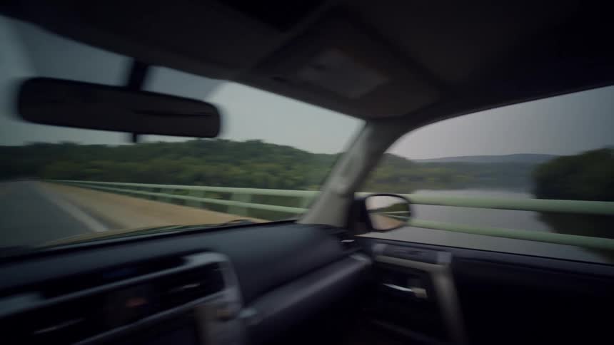 POV of a scenic drive across a river bridge through a dense forest on an overcast day