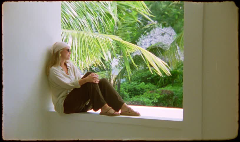 A contemplative woman enjoys a peaceful moment while sitting in a window overlooking a lush tropical garden