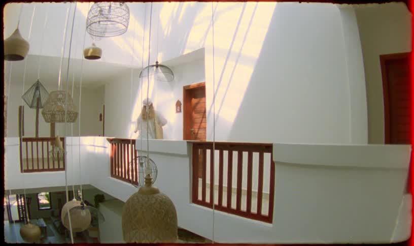 Vintage-style footage shows a stylish woman walking through the sun-drenched hallway of a modern hotel