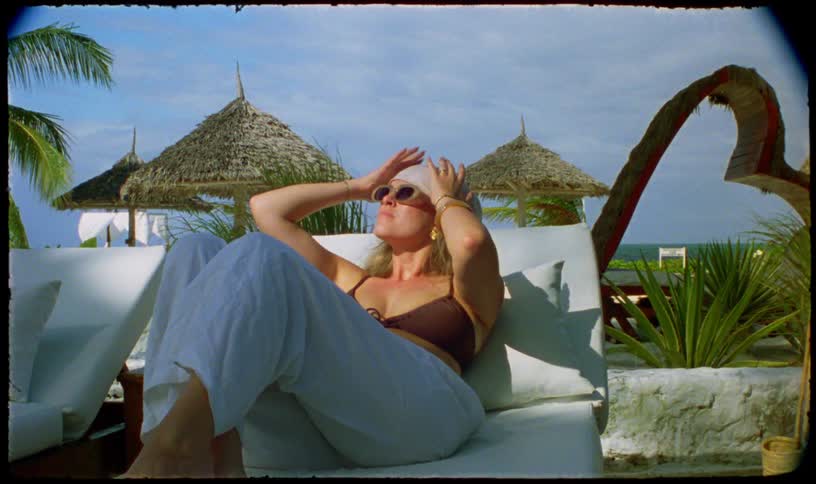A stylish blonde woman relaxes on a lounge chair while sunbathing at a beautiful tropical beach resort