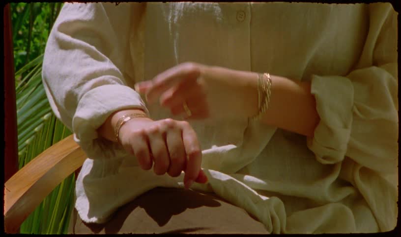 Close up of a woman's hands with gold jewelry rolling up the sleeve of her linen shirt in the sun