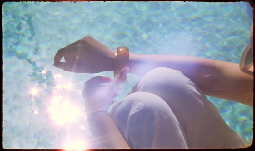A dreamy, vintage-style shot shows a person relaxing by a sparkling turquoise pool on a sunny day