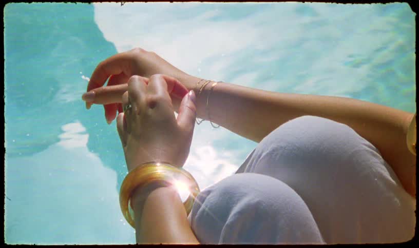 A dreamy, vintage-style shot shows a woman's hands with bracelets relaxing over the shimmering water of a sunlit pool