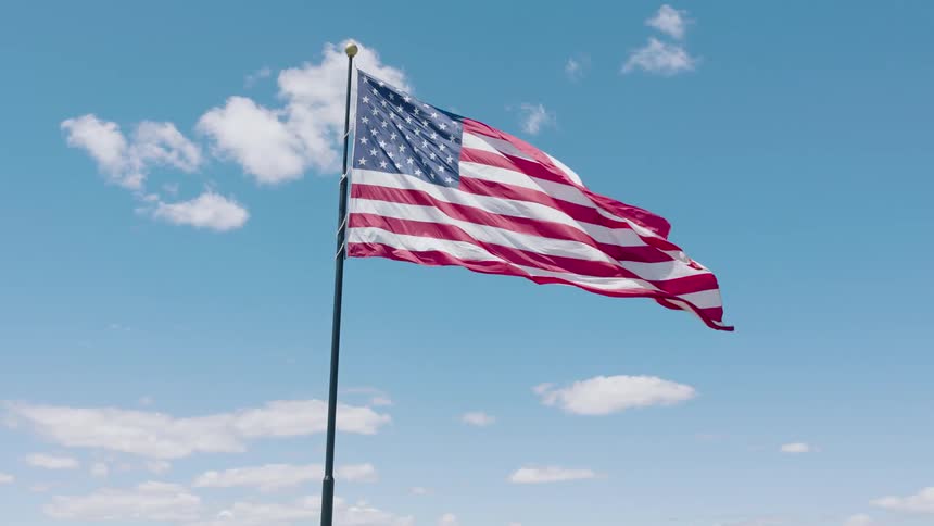 Medium clockwise orbit around the American flag waveing majestically against a blue sky with scattered clouds