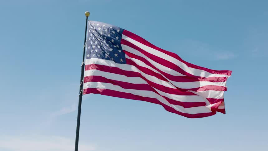 A majestic American flag waves strongly against blue sky with wisps of clouds
