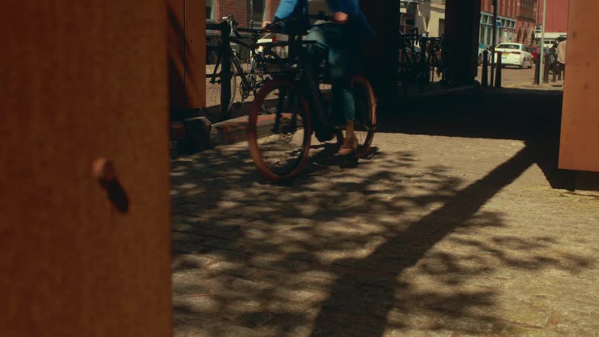 A cyclist pedals through a sun-drenched urban passageway casting long shadows on the brick pavement