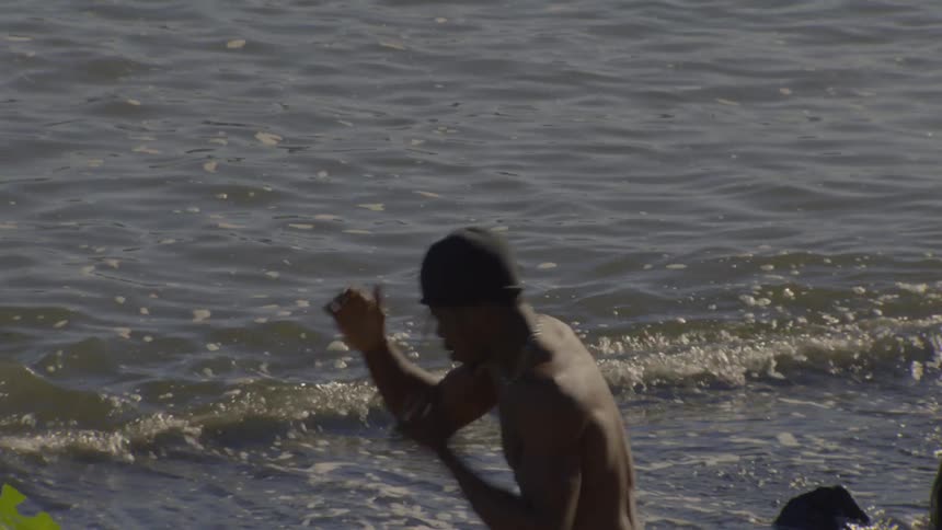 A shirtless man with his back to the camera practices shadow boxing in the ocean