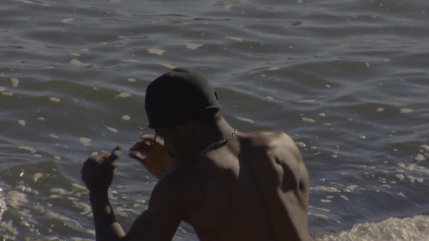 A muscular shirtless man in a beanie shadowboxes while standing in the ocean on a sunny day