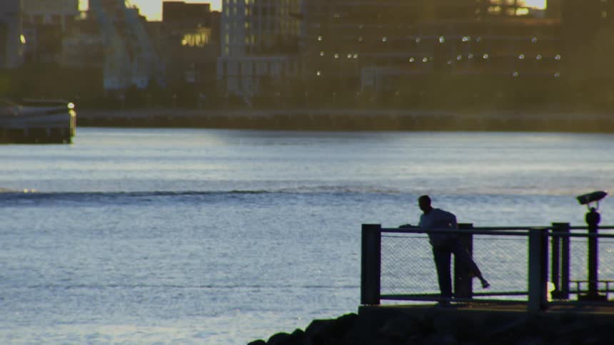 A lone figure stretches peacefully on a pier, silhouetted against the glittering water with a city in the distance