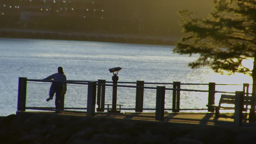 A silhouetted person contemplates the view from a pier at sunset, with golden light reflecting off the water