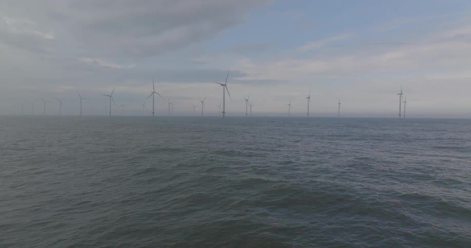 A wide shot of a massive offshore wind farm standing in the calm ocean on an overcast and cloudy day