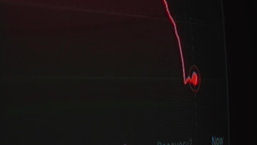 A digital screen displays a red line graph showing a dramatic stock market crash and financial recession