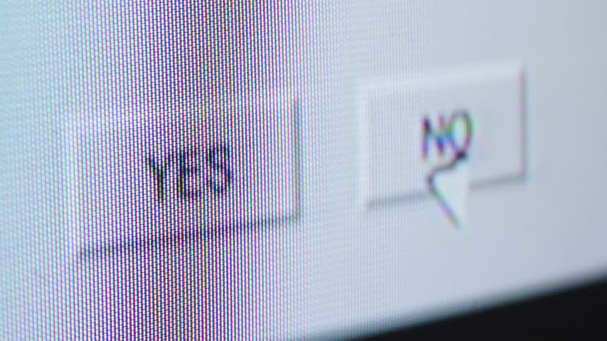 An extreme close-up of a computer screen shows a cursor hesitating between 'Yes' and 'No' before clicking 'Yes'