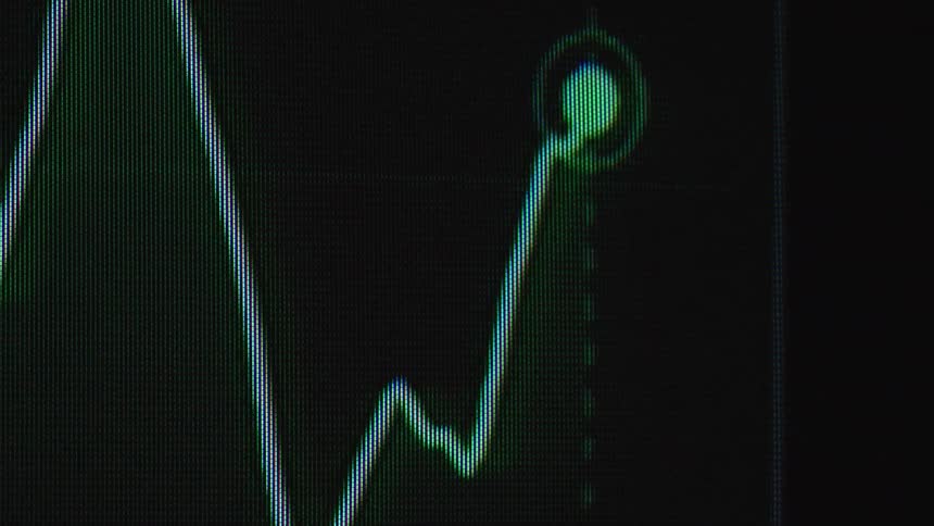 A real-time digital trading chart fluctuates on a screen, with the line graph indicating financial gains and losses